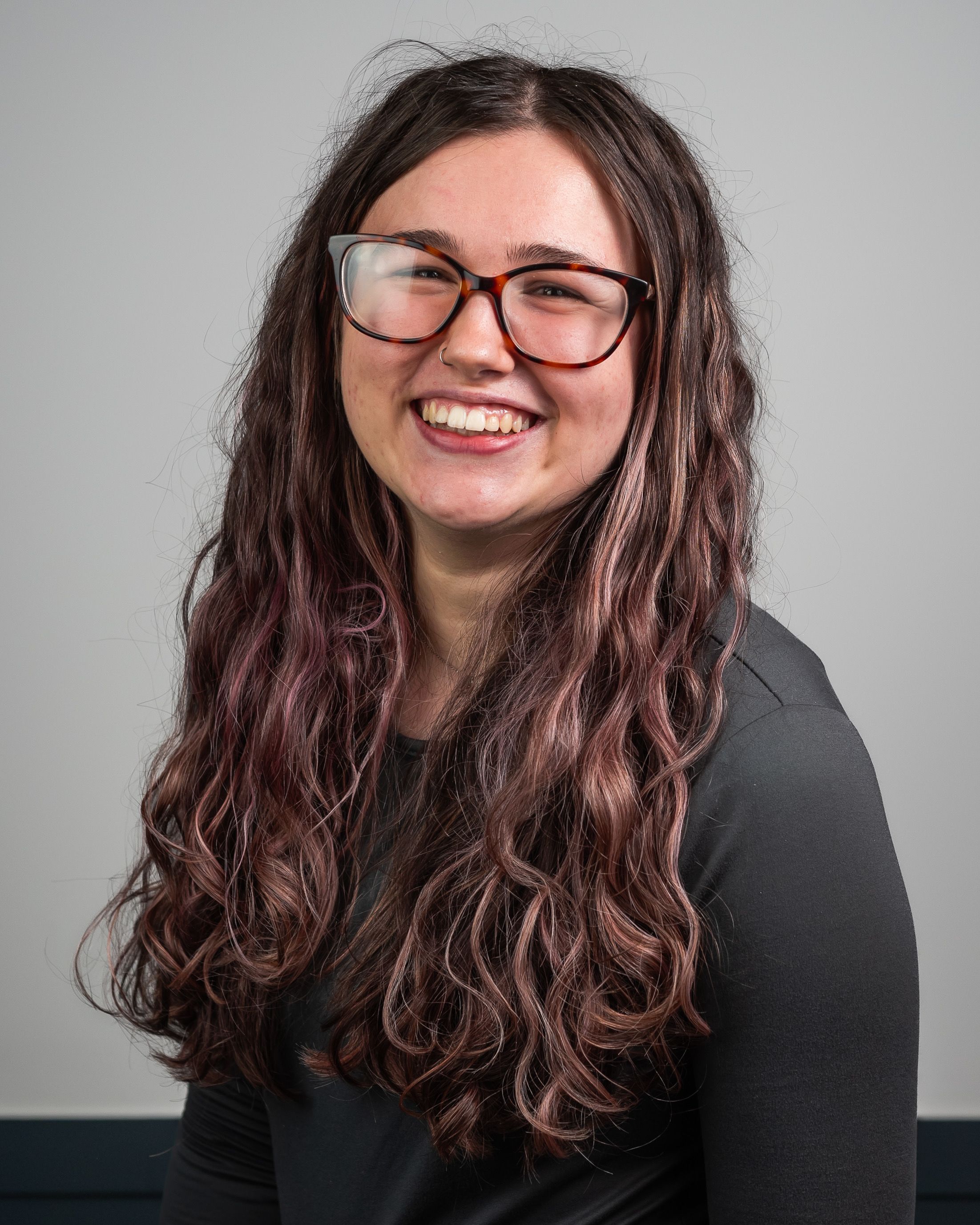 A young woman with glasses and a black shirt facing the camera directly and smiling.