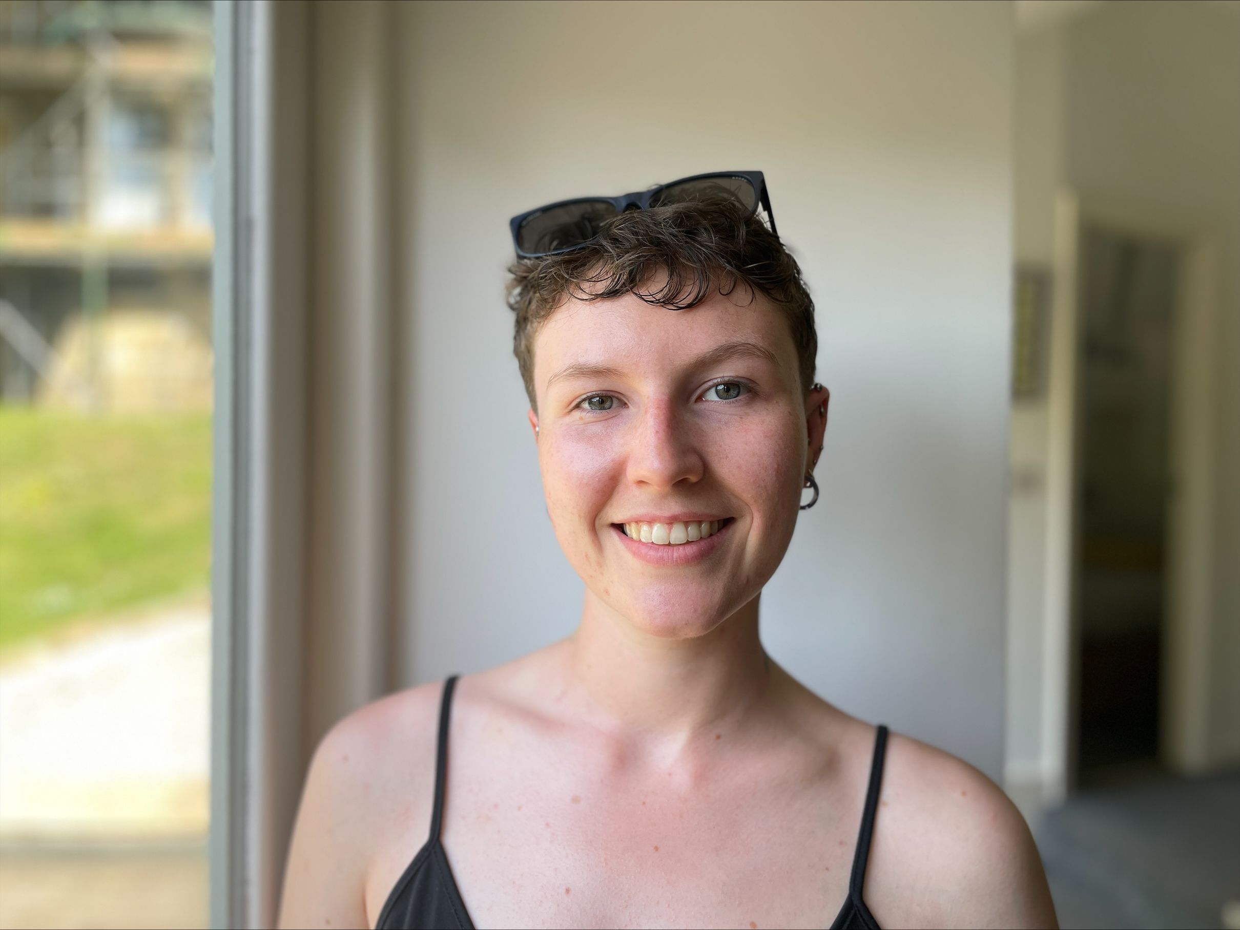 A young woman with short hair and sunglasses on her head facing the camera directly and smiling.