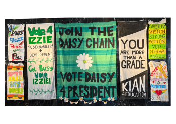 A board with a variety of banners hanging on it. The banners feature text and images, and the text reads "Vote Daisy 4 President".